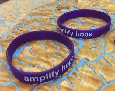 Three purple wristbands with the words amplify hope rest on a textured, metallic blue and gold surface. The top reads Recovery RoundUp: weekly inspiration. any stage. every journey. Don’t miss out—signup for your dose of encouragement.